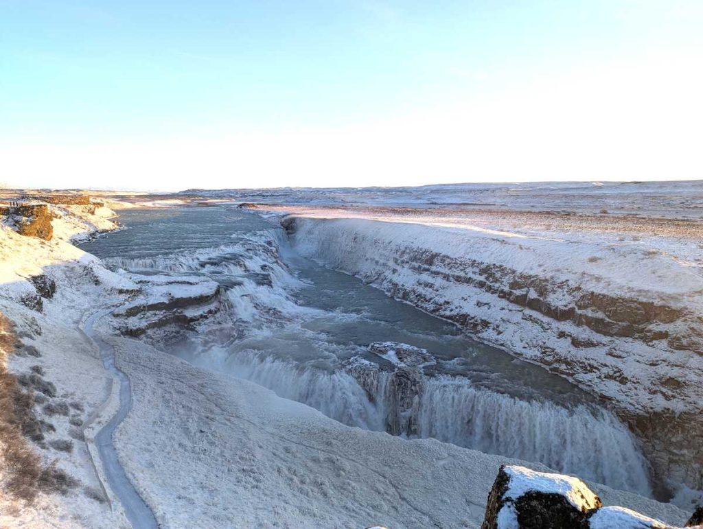 Iceland travel isn't complete with a trip to Gullfoss. Here an overhead view of the massive waterfall rushing into a canyon, with a snowy landscape all around.