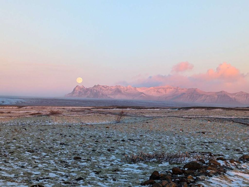 Bright pink and orange sunset over the mountains of southeastern Iceland, with a perfect full moon rising over one peak.